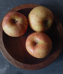 Jonagold apples in a wooden bowl, captured from a bird's eye view. Their skin displays a beautiful mix of yellow and red stripes, with visible speckles.