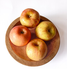 Jonagold apples in a wooden bowl, captured from a bird's eye view. Their skin displays a beautiful mix of yellow and red stripes, with visible speckles.