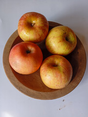 Jonagold apples in a wooden bowl, captured from a bird's eye view. Their skin displays a beautiful mix of yellow and red stripes, with visible speckles.