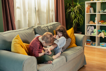 Brother tickling sister's feet on sofa in playroom: authentic family moments
