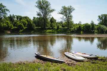 A serene river scene features neatly arranged paddleboards along the shore, offering an inviting...