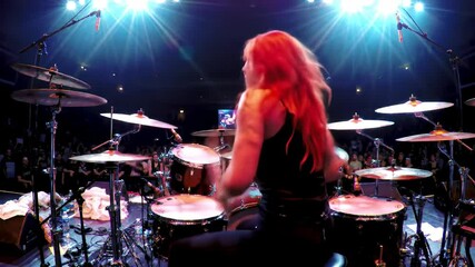 Female drummer with red hair performing energetically on stage.