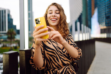 Selfie time! Beautiful woman with phone in her hands walks along the promenade with the city in the...