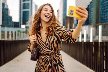 Selfie time! Beautiful woman with phone in her hands walks along the promenade with the city in the...