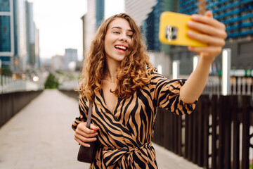 Selfie time! Beautiful woman with phone in her hands walks along the promenade with the city in the...