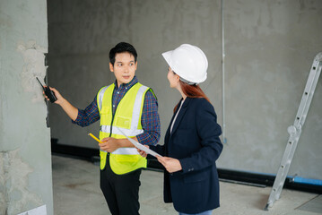 Asian engineers inspecting construction progress. Man in safety vest measures wall while female engineer
