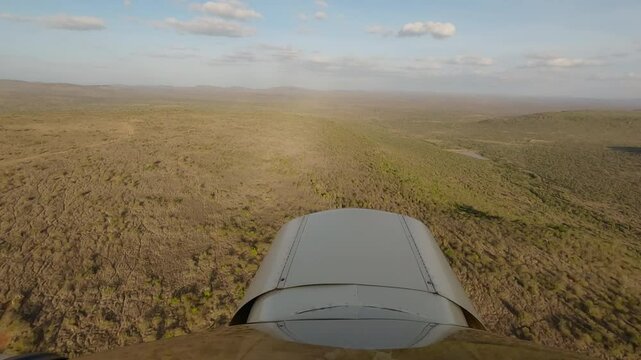 Hyperlapse of small plane flying over savannah with scattered shrubs, waterbody and valley in sunrise in Kenya