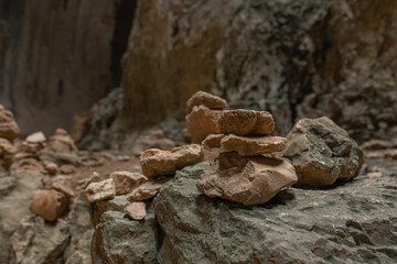 Earth-toned rock stacks line uneven cave surface. Background reveals arched rock walls and layered texture. Natural formations create peaceful pattern.
