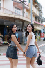 Two young women holding hands are crossing the street and turning back