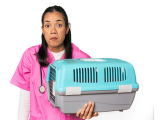 Young Filipina vet holding pet carrier shrugs shoulders and open eyes confused.