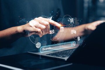 Online shopping and global e-commerce concept: Close-up of hands using a laptop with a search bar, surrounded by holographic icons representing a shopping cart, delivery truck, email, store.