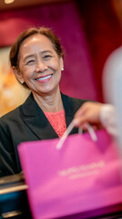 A smiling woman in a black blazer stands behind a counter, holding a pink shopping bag. The background features soft, colorful lighting, enhancing the boutique's elegance.