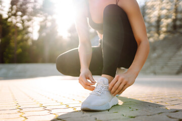 Close-up of athletic woman tying shoelaces before training. Young woman in sportswear getting ready...