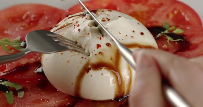 Burrata cheese with tomatoes and arugula is cut open and picked up with a fork.