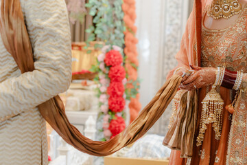 A bride and groom holding the end of a scarf together at their wedding ceremony, symbolizing unity and partnership in their new life together.