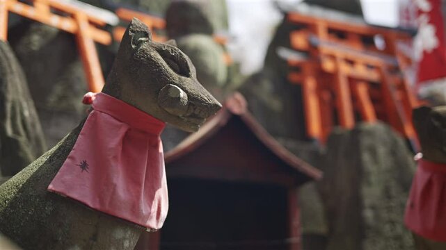 Stone fox statues adorned with red scarves at a beautiful shrine in Japan. This site showcases traditional architecture within a serene environment. Kyoto, Japan, Fushimi Inari