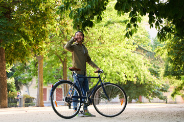 Young man talking on smartphone while holding his bicycle in park