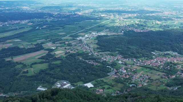 Drone panorama of the Ivrea Morainic Amphitheatre seen from Brosso, Val Chiusella, Italy, showing lush green plains, woods, and scattered villages under clear sky, high drone shot, slow motion