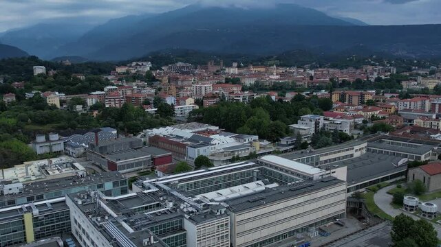 Modern glass-and-steel ICO IV building in Ivrea's Unesco-listed Olivetti district, framed by the Alps and Mount Mombarone in the background, drone shot, slow motion, sunny and cloudy sky