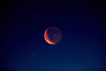 Lunar eclipse with stars and planets on the evening sky.