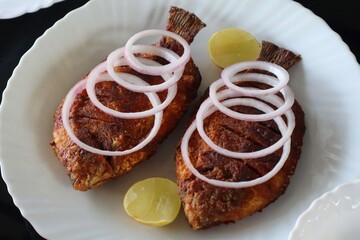 Deliciously prepared traditional South Indian fish fry served on a white plate, garnished with raw onion rings and lemon wedges. Captured in Munnar
