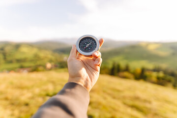 Close up of male hands holding compass against green hills. Traveler holding compass and looking direction and exploring new places outdoors. Nature concept.