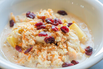  delicious and healthy oatmeal served in a white bowl. The oatmeal is topped with grated carrots, fresh apple slices, and dried red cranberries