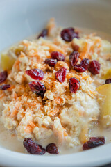  delicious and healthy oatmeal served in a white bowl. The oatmeal is topped with grated carrots, fresh apple slices, and dried red cranberries