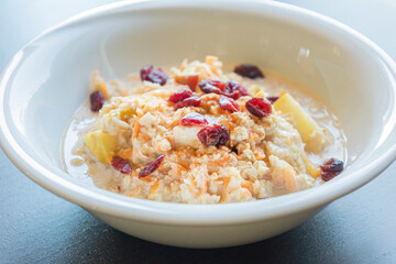  delicious and healthy oatmeal served in a white bowl. The oatmeal is topped with grated carrots, fresh apple slices, and dried red cranberries