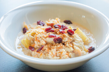  delicious and healthy oatmeal served in a white bowl. The oatmeal is topped with grated carrots, fresh apple slices, and dried red cranberries