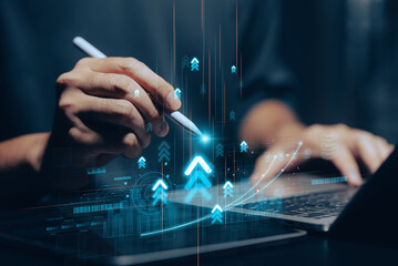 A businessman's hand points at a rising stock market graph on a laptop screen, with a digital pen indicating growth and financial success. This conceptual image illustrates investment strategies.