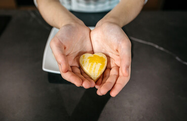 Unrecognizable female pastry chef hands holding a freshly baked heart shaped cookie with egg glaze, showcasing her passion and love for baking