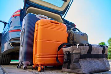 Suitcases and bags in front of open car trunk, standing on pavement near suburban house. Luggage ready for loading in vehicle before travel or moving. Concept of relocation or road trip