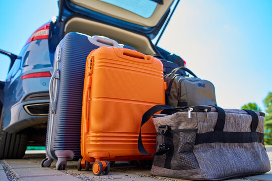 Fototapeta Suitcases and bags in front of open car trunk, standing on pavement near suburban house. Luggage ready for loading in vehicle before travel or moving. Concept of relocation or road trip