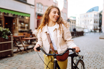 Cheerful woman with bicycle on sunny city street enjoying a walk. Tourist with bicycle walking in...