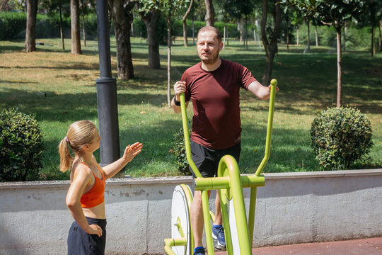 A man and a girl exercising together outdoors on a sunny day at a park. They are using an elliptical cross trainer. Promoting healthy lifestyle, fitness and family activities.