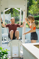 Man doing leg raises on outdoor gym equipment, guided by a female trainer.  Fitness, workout, exercise, training, healthy lifestyle, and personal training concepts. Sunny day, outdoor workout.