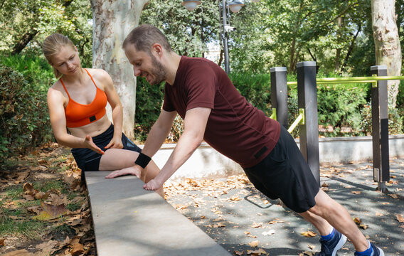 Man doing push-ups in park with female trainer. Outdoor fitness, workout, personal training session.  Healthy lifestyle, strength training, exercise. Couple exercising together. - Powered by Adobe
