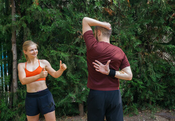 Woman assisting man with stretching exercises outdoors.  They are doing back stretches against a backdrop of lush greenery. Healthy active lifestyle.