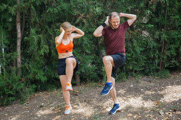 Young athletic couple doing high knees exercise outdoors in a park.  They're wearing sportswear and athletic shoes.  Healthy lifestyle and fitness concept.