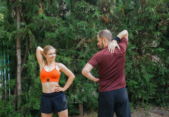 Young athletic couple stretching outdoors, warming up before workout. Man and woman in sportswear exercising together in a park. Healthy lifestyle concept.