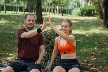 Happy sporty couple giving high five after training in a park.  Man and woman celebrating fitness success outdoors. Healthy lifestyle concept.