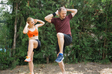 Active young couple doing high knee exercises outdoors.  Man and woman in sportswear exercising together in a park. Healthy lifestyle concept.