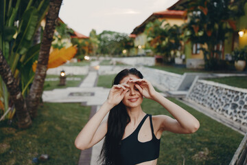 Attractive woman standing in black bra top in front of building with palm trees in background
