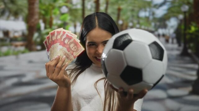 Young woman holding soccer ball and colombian pesos in an outdoor urban street setting, depicting a vibrant blend of sports and economy.