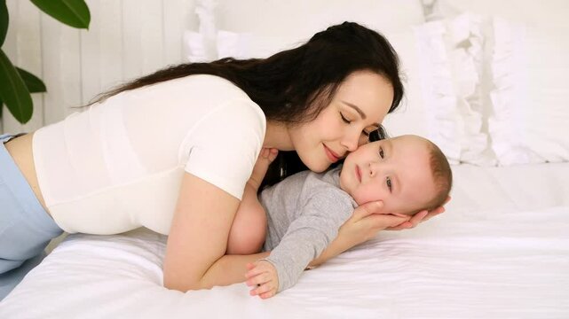 mom and baby, mother hugs and kisses baby holding him in her arms, maternal love and care, young mom having fun with baby baby, mom's decree