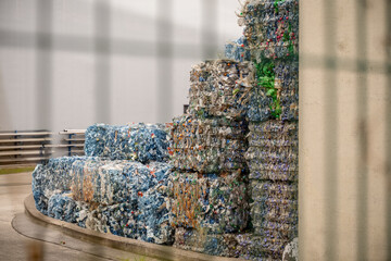 Compressed plastic bottles stacked outside recycling facility in sunlight