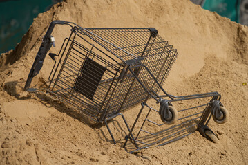 auf einem Sandhaufen liegender Einkaufswagen