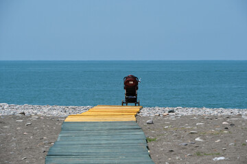 A single baby stroller on the beach of the Black Sea, Georgia. Wooden walkway to the beach with a...