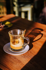 Calm morning. Still life of empty coffee cup. Empty glass coffee cup with milk foam remnants sits in sunlight on wooden cafe table, casting a soft shadow. Concept of coffee break, cozy moment